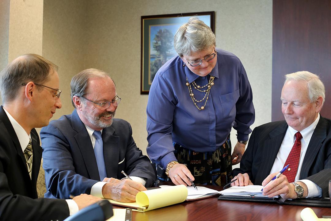 Four individuals seated at a table, focused on signing documents together.